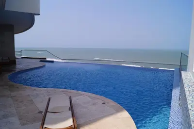 a swimming pool with two chairs next to the ocean at Beach front Apartament in Cartagena de Indias
