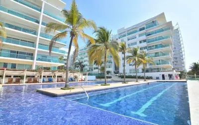 a swimming pool with palm trees in front of a building at Amplio apt de 3 alcobas edificio primera linea de playa in Cartagena de Indias
