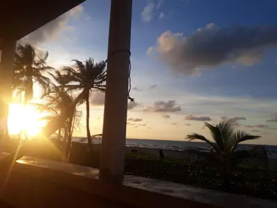 a sunset from a balcony with palm trees and the ocean at Cabaña Playa De Los Venados in San Bernardo del Viento