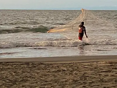 a man walking into the ocean with a net at Zéfiro Hostal in San Bernardo del Viento