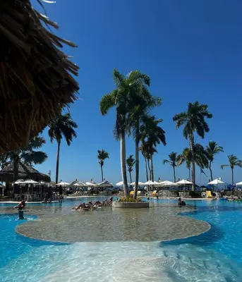 a pool with palm trees and people in the water at Zuana Beach Resort in Santa Marta