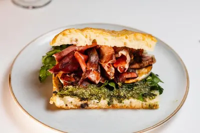 a white plate with a sandwich with meat and greens at Casa Franco Hotel in Cartagena de Indias