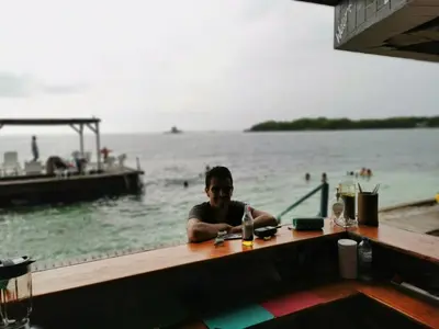 a man sitting at a table in front of the water at Rosario EcoHotel - Islas del Rosario in Isla Grande