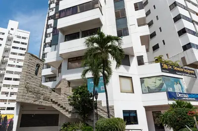 a tall white building with a palm tree in front of it at Apartamento en Bocagrande - Piscina, Jacuzzi y Mar in Cartagena de Indias