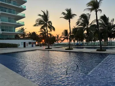 a pool at the beach with palm trees and a building at Hermoso apartamento en la mejor zona de la ciudad in Cartagena de Indias