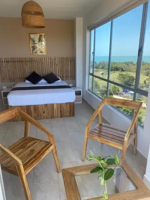 a bedroom with a bed and chairs and a large window at Hotel Bahia Rada in Moñitos