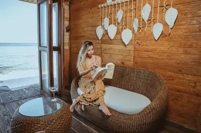 a woman sitting in a wicker chair reading a book at Hotel Prana Beach in Baru