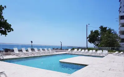 a swimming pool with lounge chairs and the ocean at Apartamento El Laguito Cartagena in Cartagena de Indias