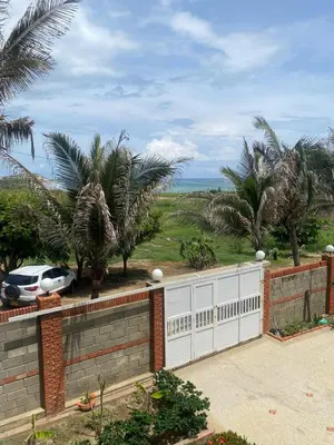a house with a fence and palm trees and the ocean at Villa frente al Mar cerca a Barranquilla in Tubará