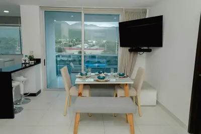 a dining table and chairs in a living room with a television at Hermoso apartamento. Cerca del mar. in Santa Marta