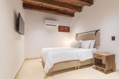 a white bedroom with a bed and a tv at Hotel Voilá Getsemaní in Cartagena de Indias