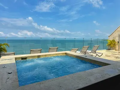 a swimming pool with chairs and the ocean in the background at ¡Amazing Beach Dúplex! Infinity Pool / Rooftop in Cartagena de Indias