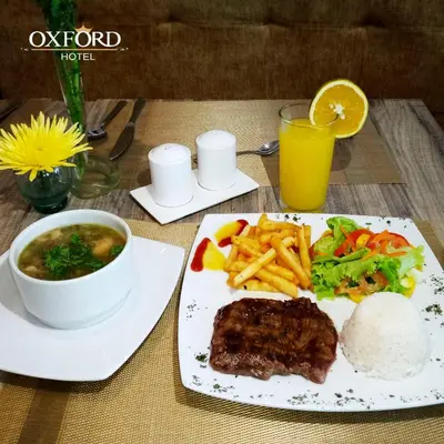 a plate of food with meat and french fries and a drink at Hotel Oxford Barranquilla in Barranquilla
