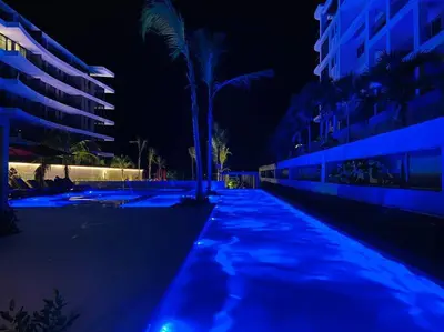 a blue lighted pathway with a palm tree and buildings at Fantastic Loft/Beachfront+Pools in Cartagena de Indias